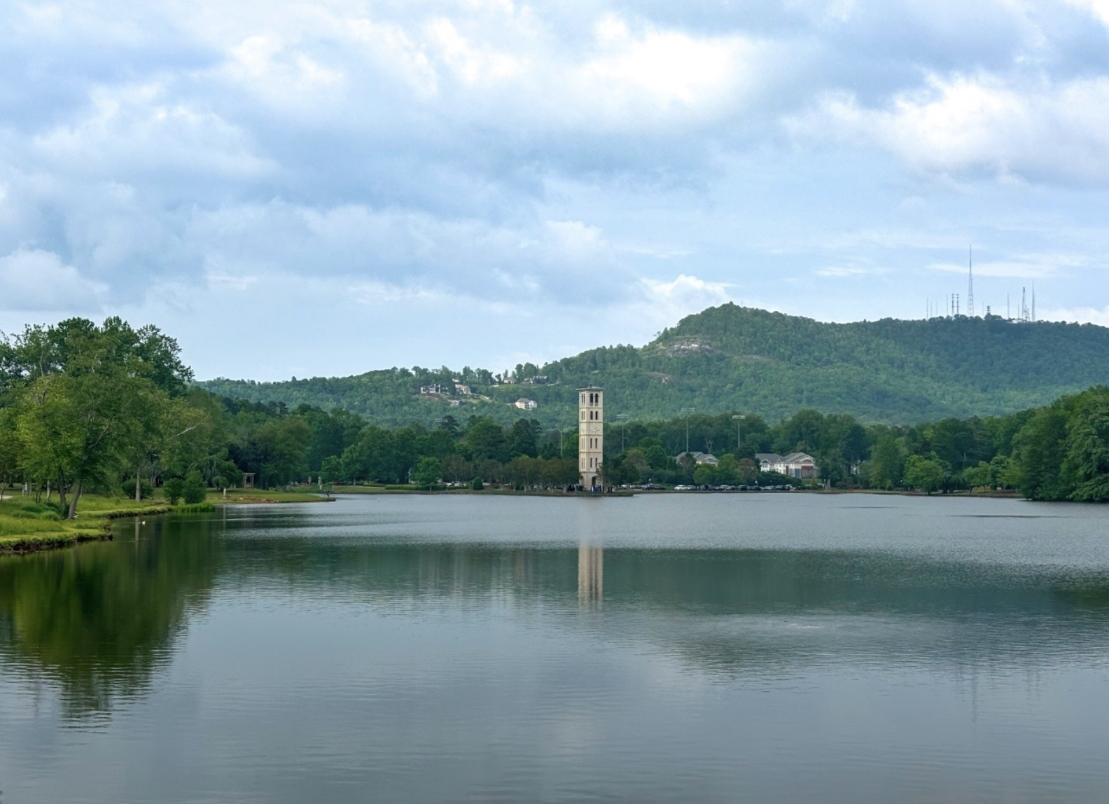 Clock tower across a still lake beneath a cloudy sky