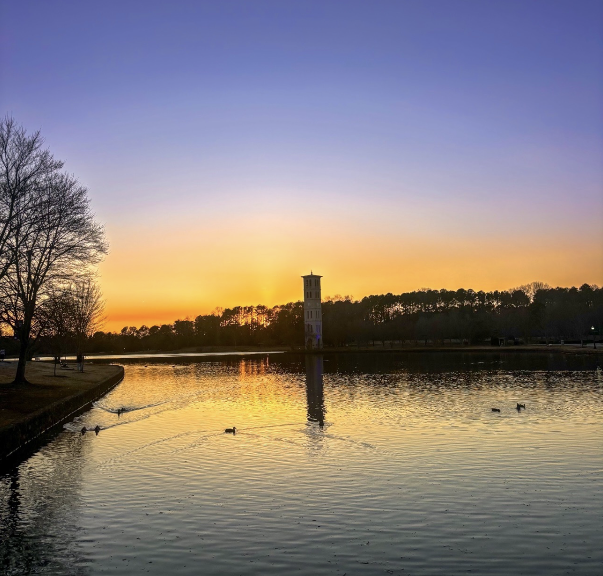 Bell tower silhouetted against an orange sunset over a lake